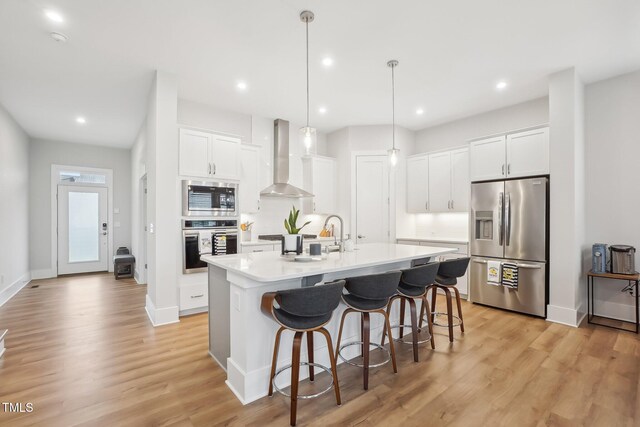 5616 Horsewalk Cir, Raleigh, NC 27606 - kitchen featuring wall chimney range hood, white cabinetry, a breakfast bar, appliances with stainless steel finishes, and a center island with sink