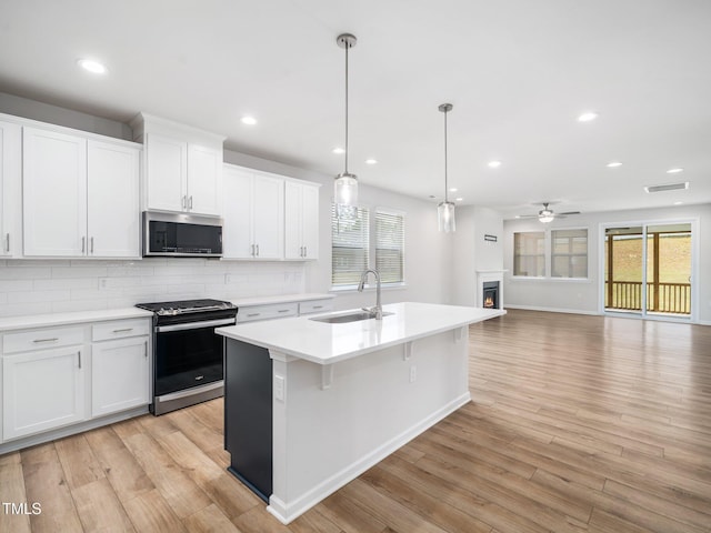 kitchen featuring stainless steel microwave, a sink, visible vents, gas range oven, and light wood-style floors