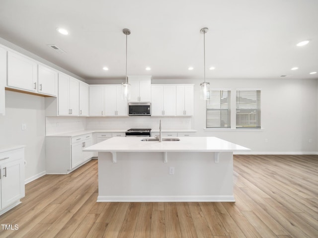 kitchen with a sink, stainless steel appliances, light countertops, light wood-style floors, and decorative backsplash