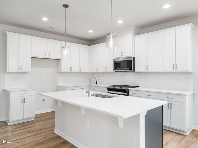 kitchen featuring light wood finished floors, a sink, white cabinetry, stainless steel appliances, and tasteful backsplash