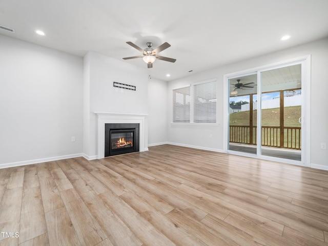 unfurnished living room with light wood finished floors, a ceiling fan, a glass covered fireplace, and visible vents