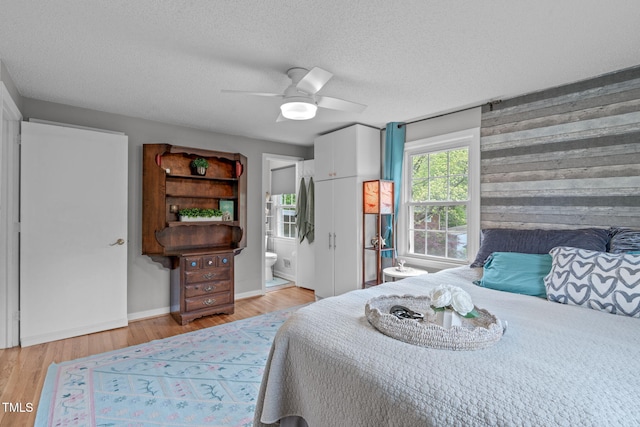 bedroom featuring ensuite bath, ceiling fan, light wood-type flooring, and a textured ceiling