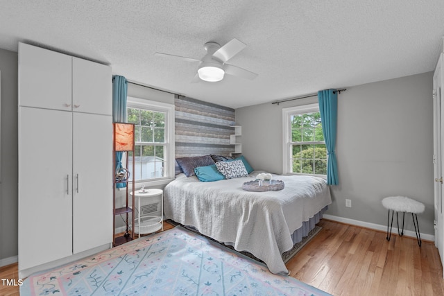 bedroom featuring baseboards, light wood finished floors, an accent wall, and multiple windows