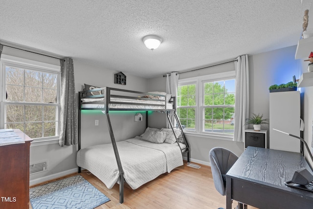 bedroom with baseboards, visible vents, multiple windows, and wood finished floors