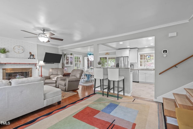 living room featuring ornamental molding, a ceiling fan, stairs, and a brick fireplace