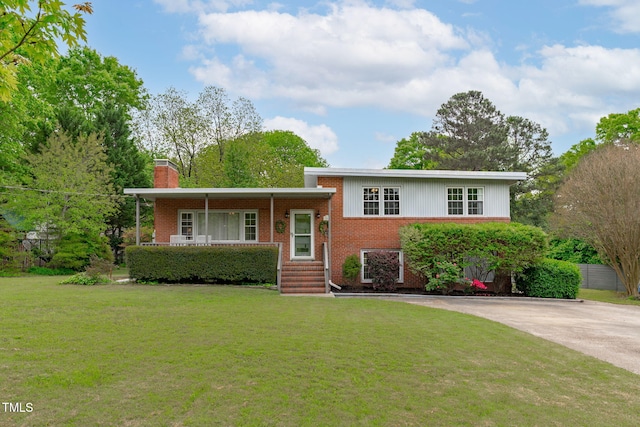split level home with a chimney, concrete driveway, a front lawn, and brick siding