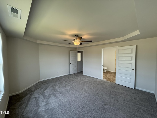 unfurnished bedroom featuring a tray ceiling, ensuite bathroom, visible vents, baseboards, and carpet