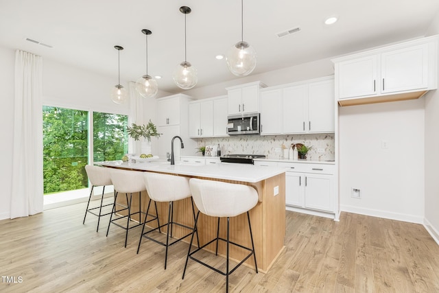 111 Silver Moon Ln Unit 121, Clayton, NC 27527 - kitchen with stainless steel microwave, tasteful backsplash, visible vents, stove, and an island with sink