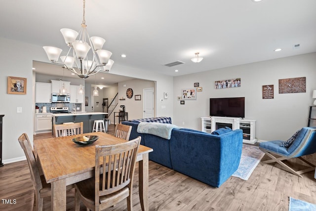 dining room with visible vents, light wood finished floors, an inviting chandelier, and stairs