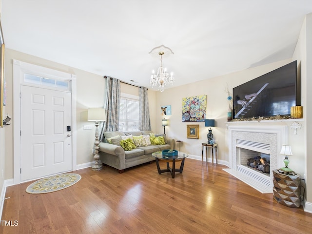 living area with a chandelier, wood finished floors, baseboards, and a fireplace with flush hearth