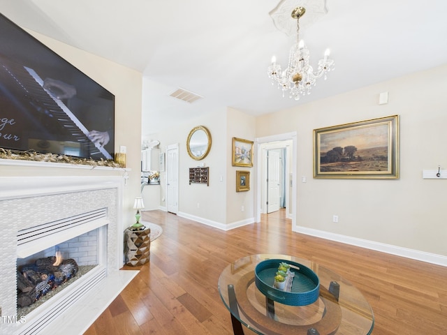 living room featuring a chandelier, a warm lit fireplace, wood finished floors, and visible vents