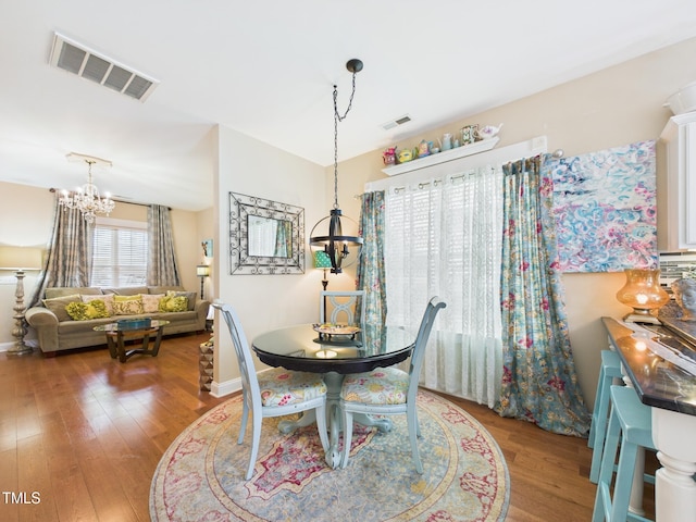 dining space featuring baseboards, wood finished floors, visible vents, and a notable chandelier