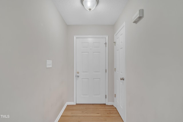 corridor featuring baseboards, a textured ceiling, and light wood-style floors