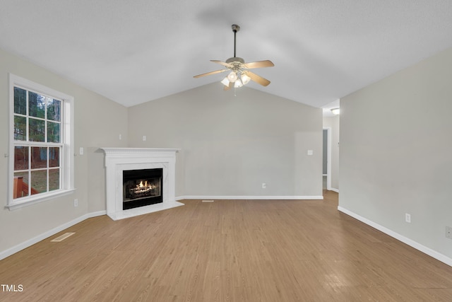 unfurnished living room featuring light wood-style flooring, visible vents, baseboards, a ceiling fan, and a lit fireplace