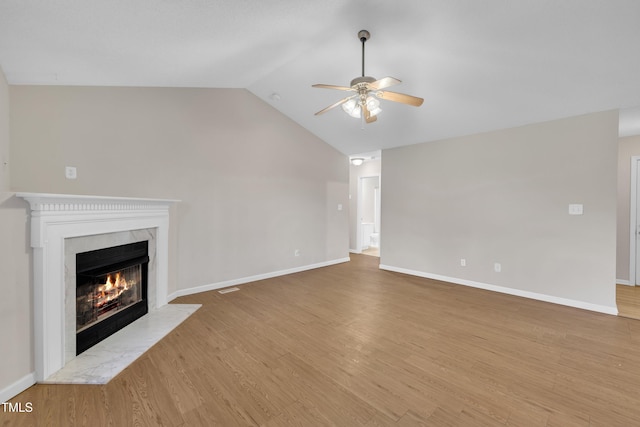 unfurnished living room with vaulted ceiling, wood finished floors, a premium fireplace, baseboards, and ceiling fan