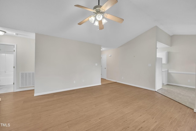 empty room featuring a ceiling fan, lofted ceiling, baseboards, visible vents, and light wood-style floors