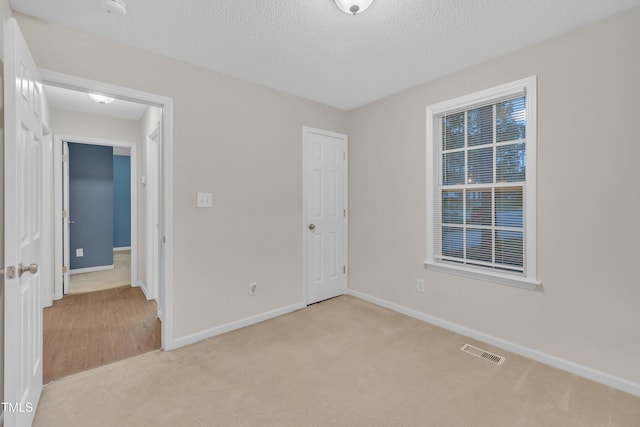 unfurnished bedroom featuring carpet, baseboards, a textured ceiling, and visible vents