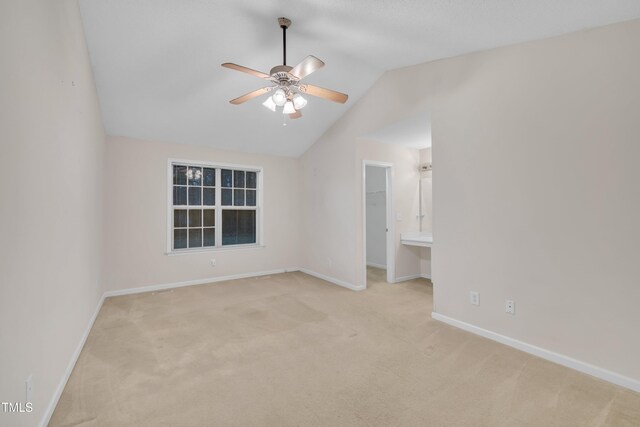 empty room featuring a ceiling fan, light carpet, baseboards, and vaulted ceiling