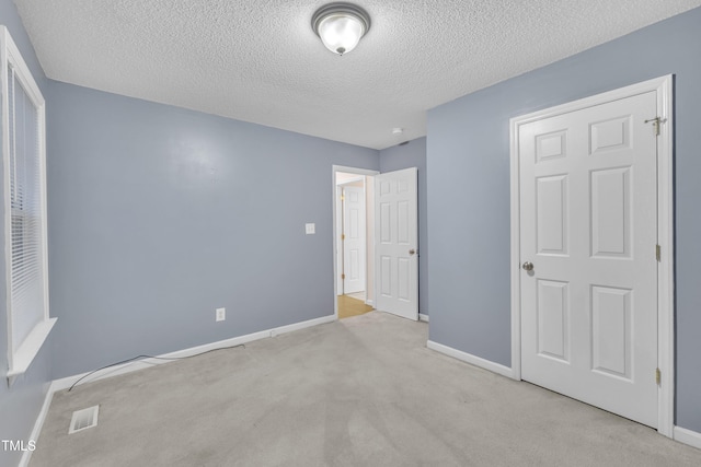 unfurnished bedroom featuring baseboards, carpet flooring, a textured ceiling, and visible vents
