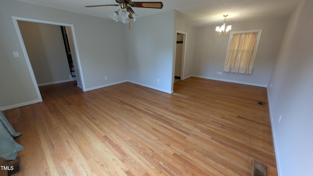 spare room with light wood-style floors, baseboards, ceiling fan with notable chandelier, and visible vents