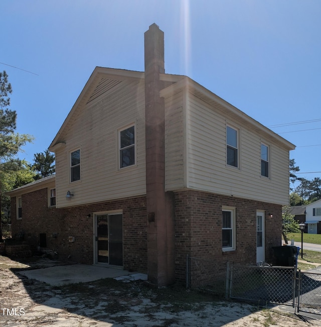 view of home's exterior featuring fence, a patio, a chimney, and brick siding
