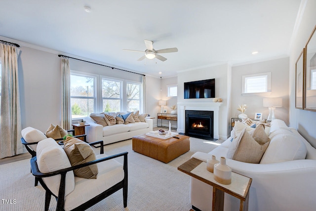 living area with crown molding, a ceiling fan, a lit fireplace, and a healthy amount of sunlight
