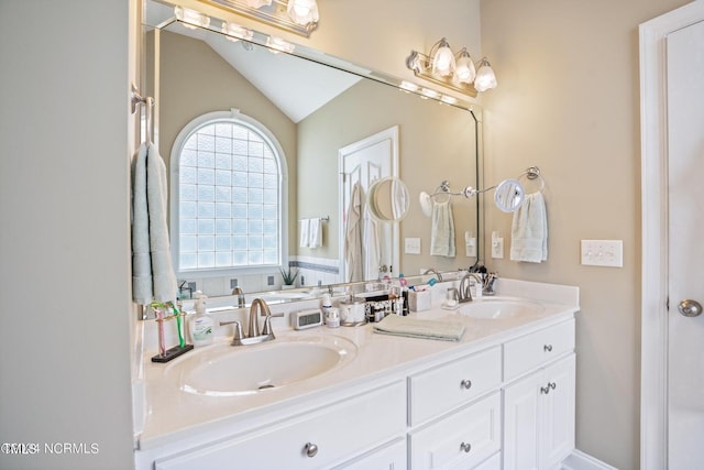 bathroom with lofted ceiling, a sink, and double vanity