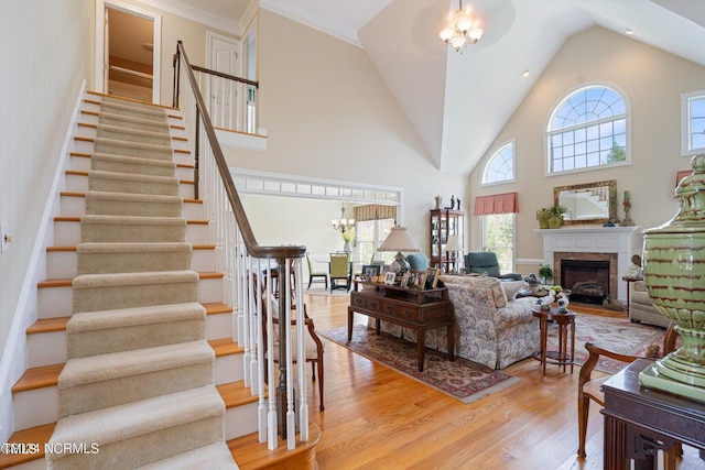 living area featuring stairway, a premium fireplace, an inviting chandelier, high vaulted ceiling, and light wood-style floors