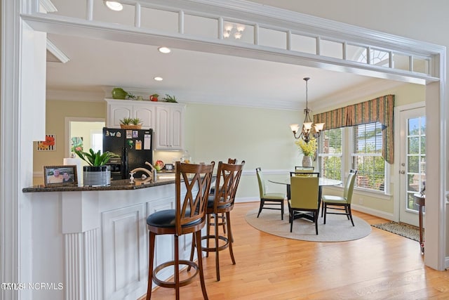 kitchen with crown molding, black fridge, dark stone counters, white cabinets, and light wood-style flooring