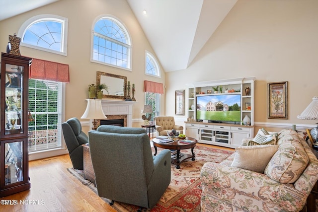 living area featuring a high end fireplace, high vaulted ceiling, a healthy amount of sunlight, and wood finished floors