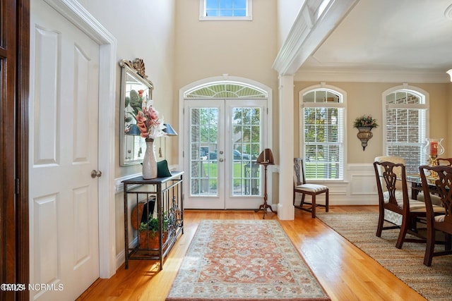 entryway with wood finished floors, french doors, crown molding, and wainscoting