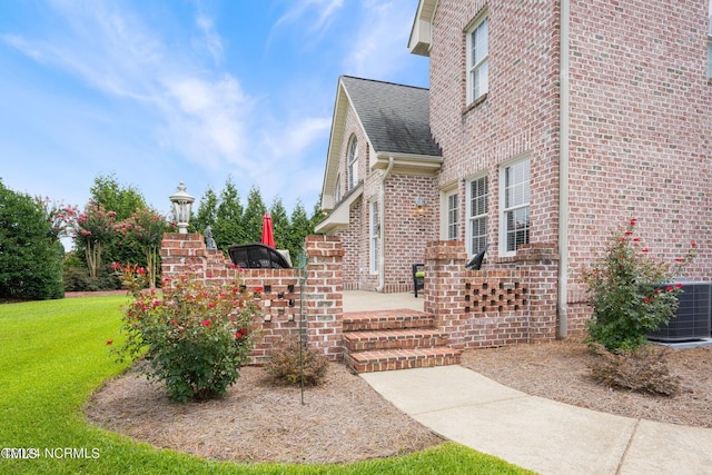 view of side of home featuring cooling unit, brick siding, a yard, and roof with shingles
