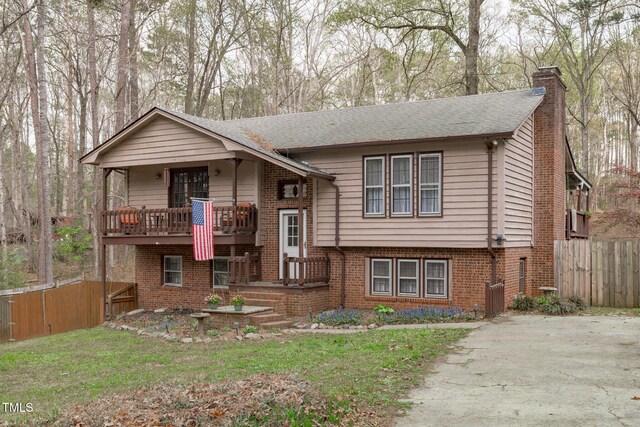 split foyer home featuring a balcony, fence, a chimney, a front yard, and brick siding