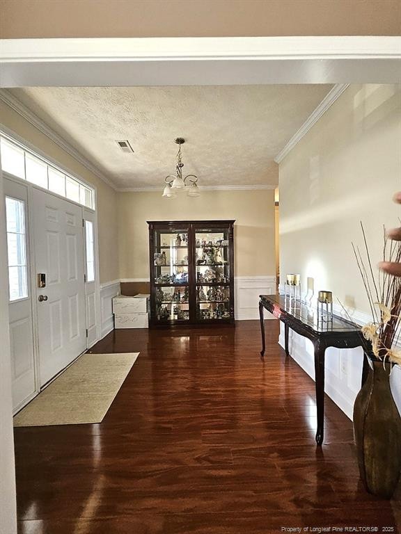entryway with an inviting chandelier, crown molding, wood finished floors, and visible vents