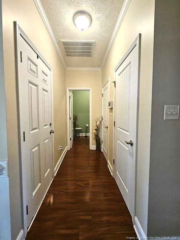 corridor featuring a textured ceiling, baseboards, wood finished floors, visible vents, and ornamental molding