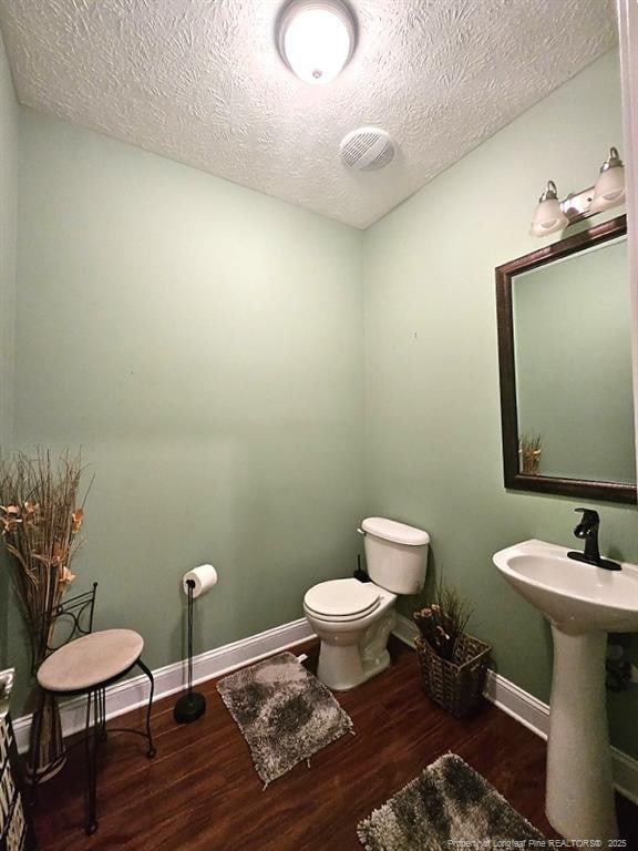 half bath featuring a sink, toilet, a textured ceiling, baseboards, and wood finished floors