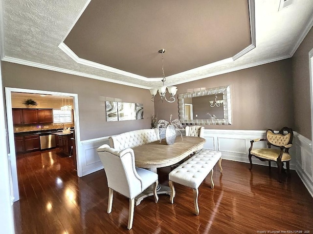 dining space featuring dark wood-style flooring, a notable chandelier, a decorative wall, a wainscoted wall, and a tray ceiling