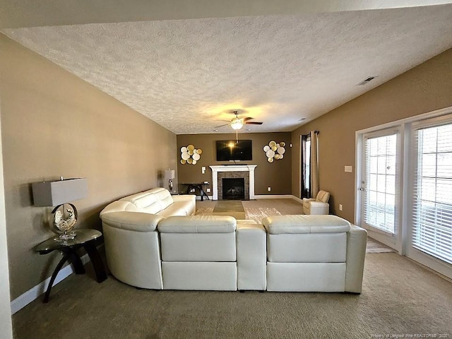 living room featuring ceiling fan, a textured ceiling, a fireplace, carpet floors, and baseboards