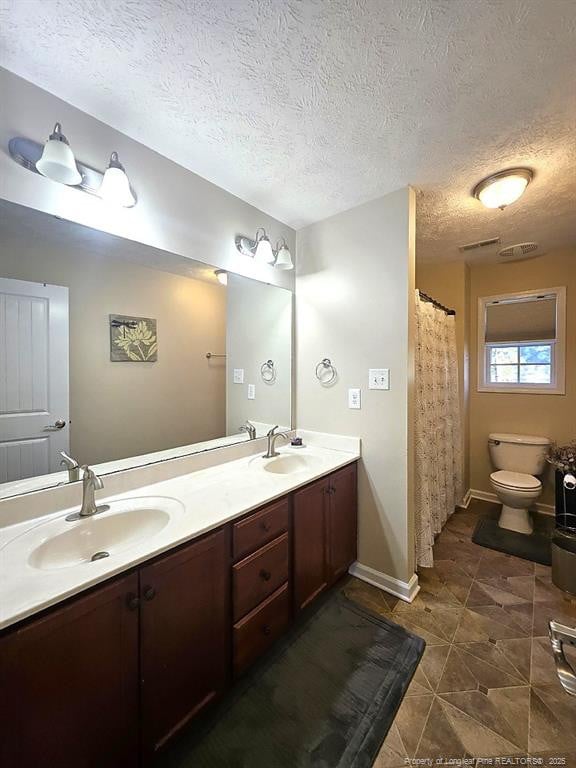 bathroom with double vanity, toilet, a textured ceiling, and a sink
