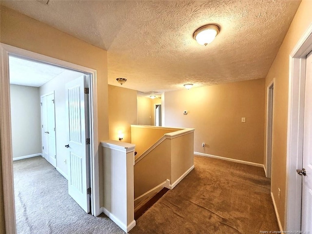 hallway with baseboards, carpet flooring, a textured ceiling, and an upstairs landing