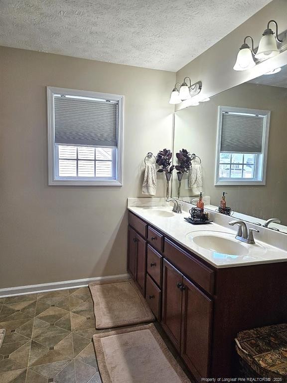 bathroom featuring a sink, baseboards, a textured ceiling, and double vanity