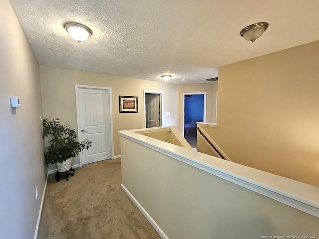 hall featuring carpet flooring, a textured ceiling, baseboards, and an upstairs landing