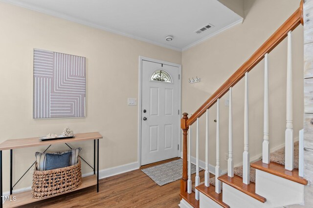 entryway featuring stairs, crown molding, wood finished floors, baseboards, and visible vents
