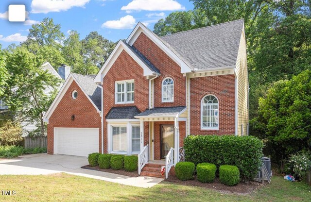 traditional home with brick siding, a front lawn, concrete driveway, an attached garage, and a shingled roof