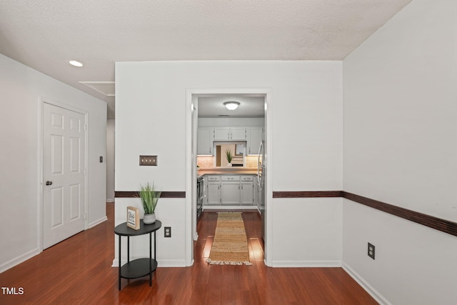 hallway featuring attic access, dark wood-style floors, baseboards, and a textured ceiling