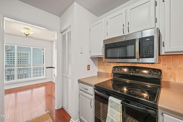 kitchen featuring stainless steel microwave, black electric range, white cabinetry, and a textured ceiling