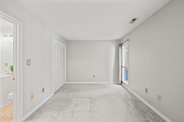 unfurnished bedroom with a sink, baseboards, light colored carpet, and visible vents