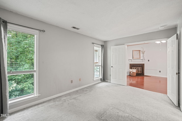 interior space featuring carpet flooring, a fireplace with flush hearth, baseboards, a textured ceiling, and visible vents