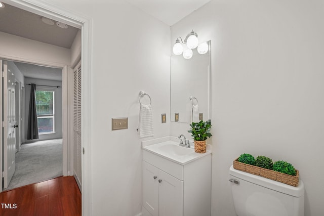 half bath featuring wood finished floors, toilet, and vanity