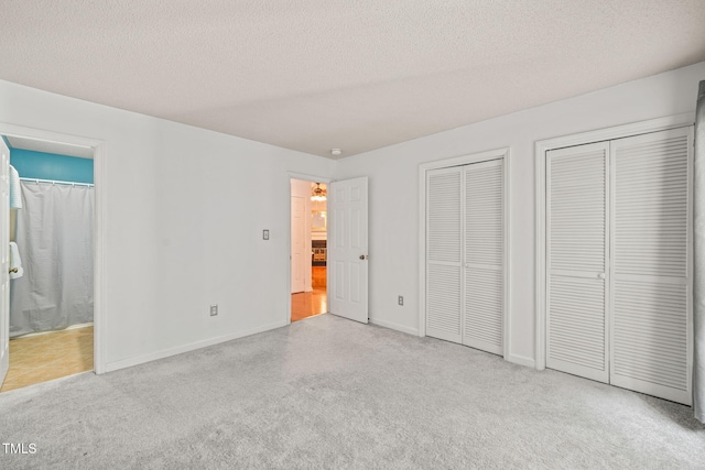 unfurnished bedroom with baseboards, multiple closets, a textured ceiling, and connected bathroom